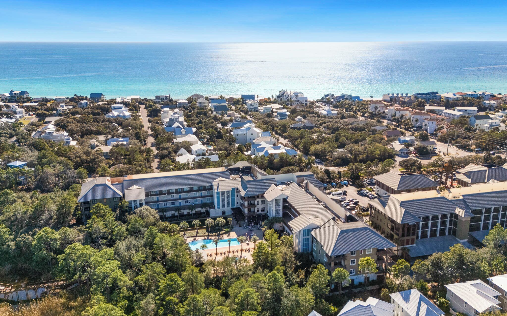 Vista aérea de uma área residencial costeira com casas, um edifício grande com piscina e vista para o oceano.