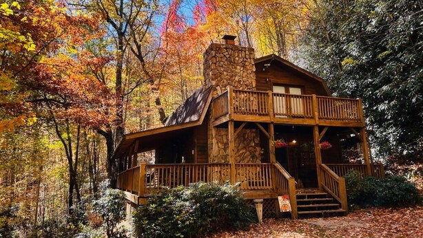 Une cabane rustique avec une cheminée en pierre, une terrasse en bois et un porche.