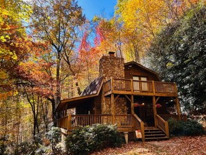 A rustic cabin with a stone chimney, wooden deck, and a porch.