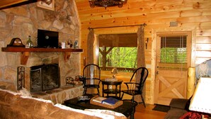 L’intérieur chaleureux d’un chalet avec une cheminée en pierre, des murs en bois et une grande fenêtre donnant sur la forêt.