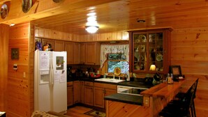 Une cuisine rustique aménagée dans une cabane en bois, avec un réfrigérateur, des placards en bois, un évier et une fenêtre avec des rideaux.