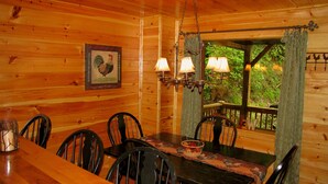 Une salle à manger aménagée dans une cabane en bois, avec une table, des chaises et deux lampes fixées au mur.