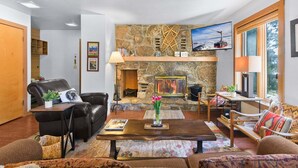 Ein gemütliches Wohnzimmer mit Kamin aus Stein, einer Ledersofa und einem Fernseher.