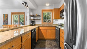 Eine moderne Küche mit Granit-Arbeitsplatten, Holzschränken, Edelstahlgeräten und einem Fenster, das für natürliches Licht sorgt.