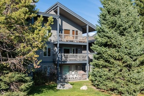 Stunning two-story residence with a spacious balcony and a central entrance, set amidst a serene lawn and lush evergreen trees.