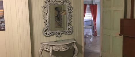 A hallway with a decorative mirror, a console table, and a door leading to another room.