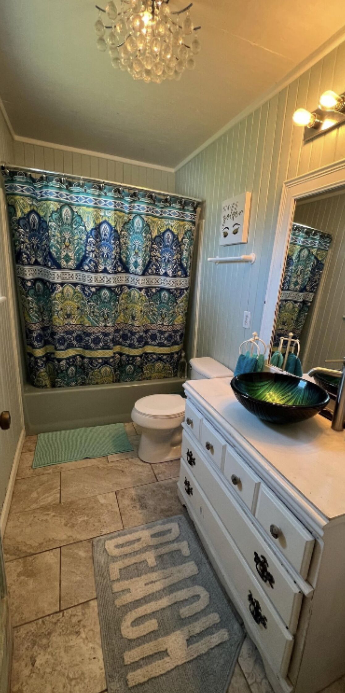 A bathroom with a patterned shower curtain, a toilet, a sink with a bowl, and a chandelier.