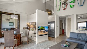 A modern living room with a dining area, a kitchen, and a large TV screen. - 1 Of Largest 2 Bedroom Units, 1 Of Highest # of 5 Star Reviews,Picture Sunsets. (Kihei)