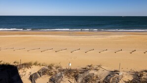 Ein weiter Sandstrand mit Holzlattenzaun und einem Schild.