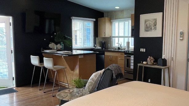 Ein modernes Schlafzimmer mit einem großen Bett, einem kleinen Schreibtisch und einer Küchenzeile im Hintergrund.