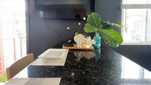 Eine moderne Küche mit schwarzer Granitabdeckung, einem flachbildfernseher an der Wand und einer großen, grünen Pflanze in einer blauen Vase.