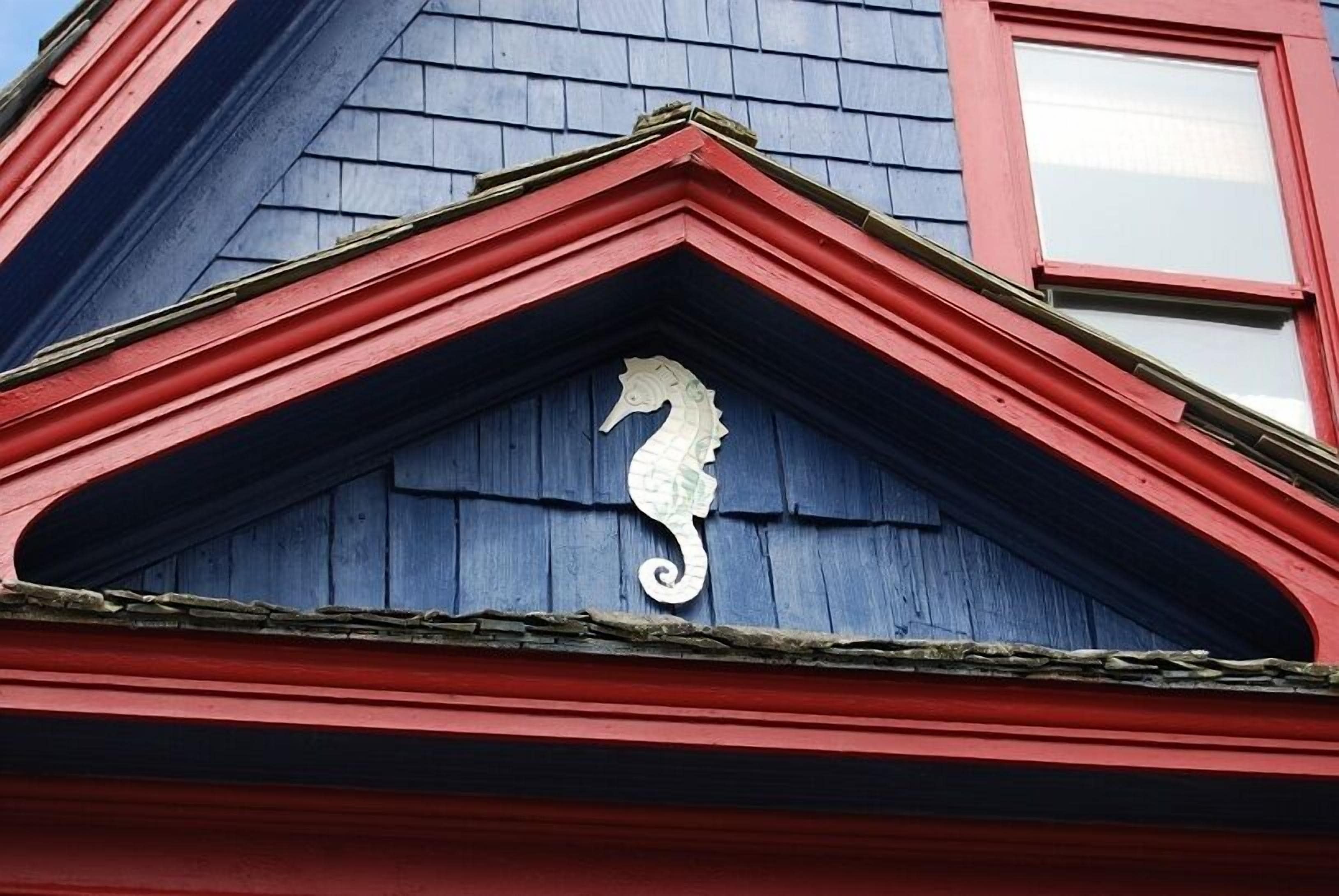 Een gebouw met een rode en blauwe gevel, voorzien van een decoratief zeepaard op de dakschild.