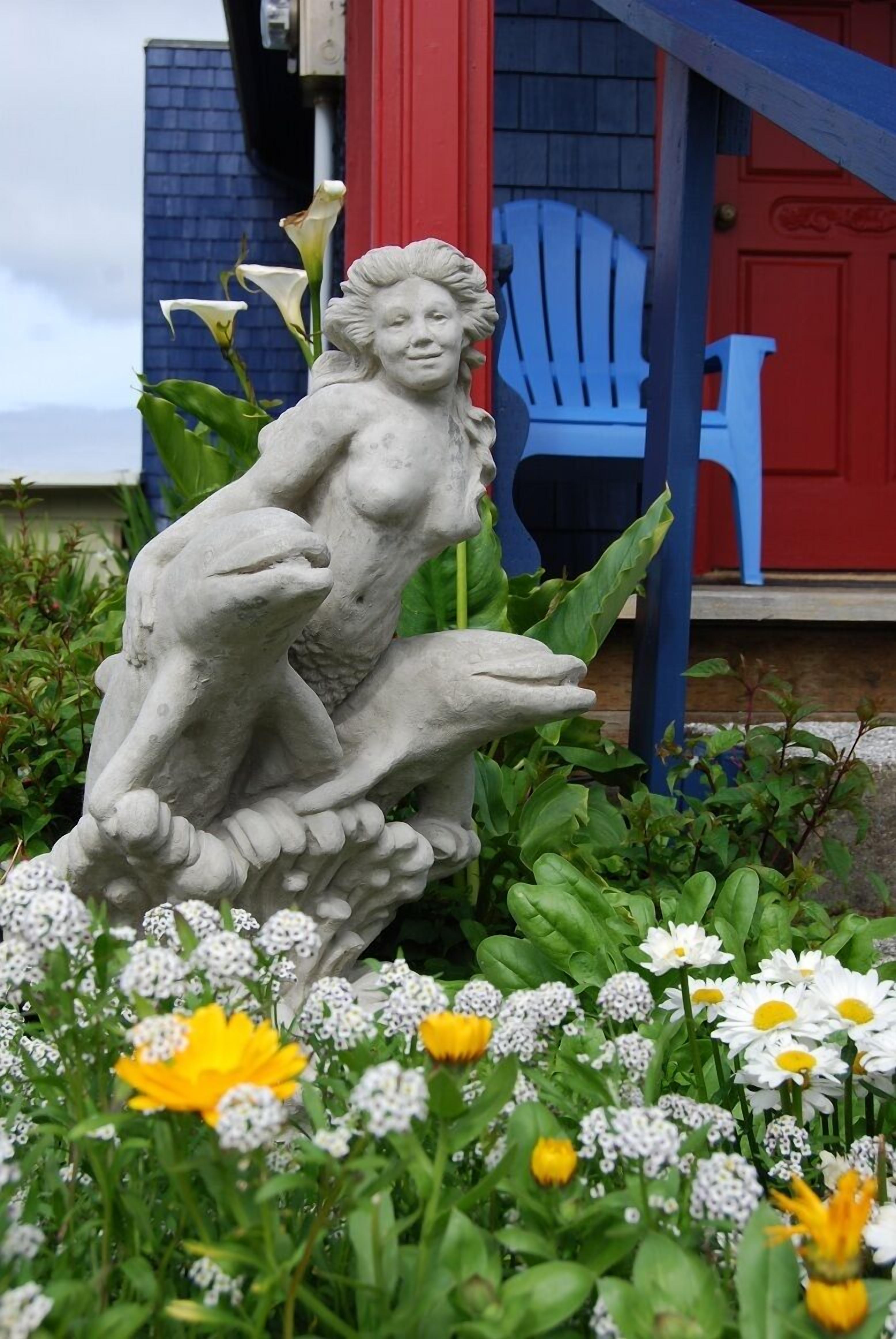 A garden with a stone sculpture of a woman and a frog, surrounded by various flowers.