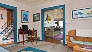 Una sala de estar con un piano, un sofá, un sillón de mimbre y un comedor con mesa y sillas.