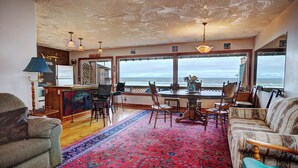 Un espacio habitable amplio con un gran ventanal con vista al océano, una mesa de comedor con sillas y una zona de estar acogedora con un tapete estampado.