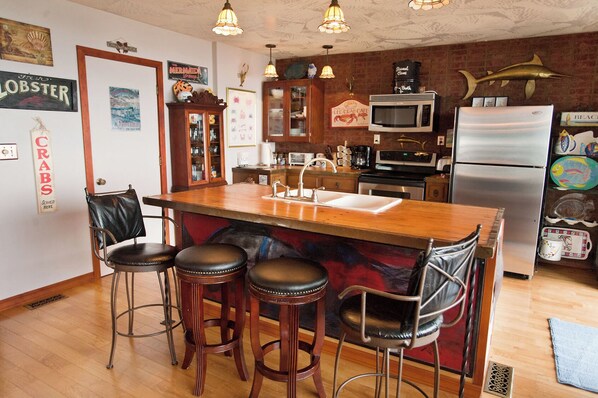 A kitchen with a wooden island, bar stools, a refrigerator, and various kitchen appliances.