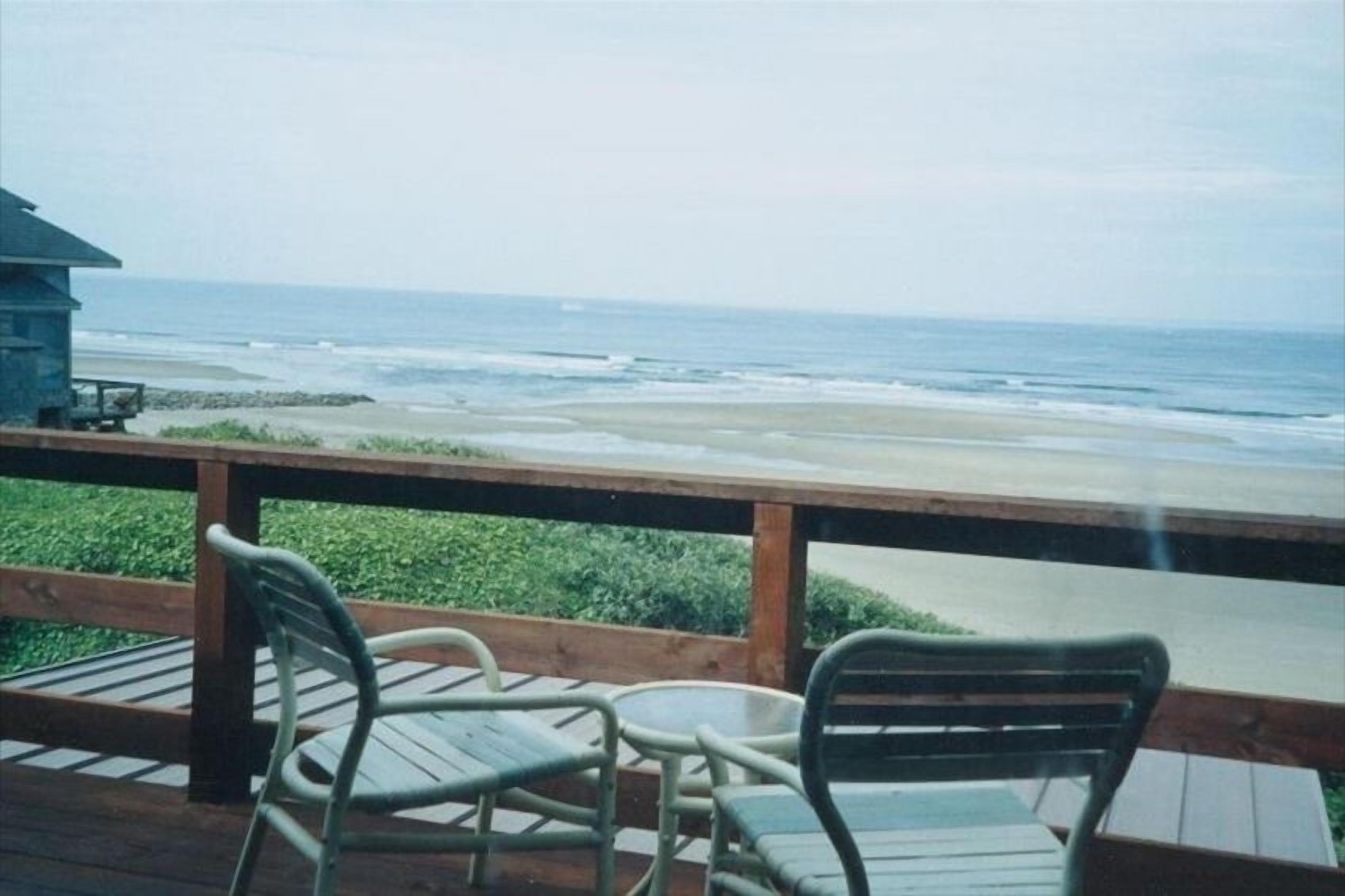A wooden deck with two chairs and a table overlooking a beach.
