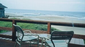 Una terraza de madera con dos sillas y una mesa, con vista a la playa.