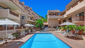 Ein Schwimmbecken mit Liegestühlen und Sonnenschirmen, umgeben von mehrstöckigen Gebäuden mit Balkonen.