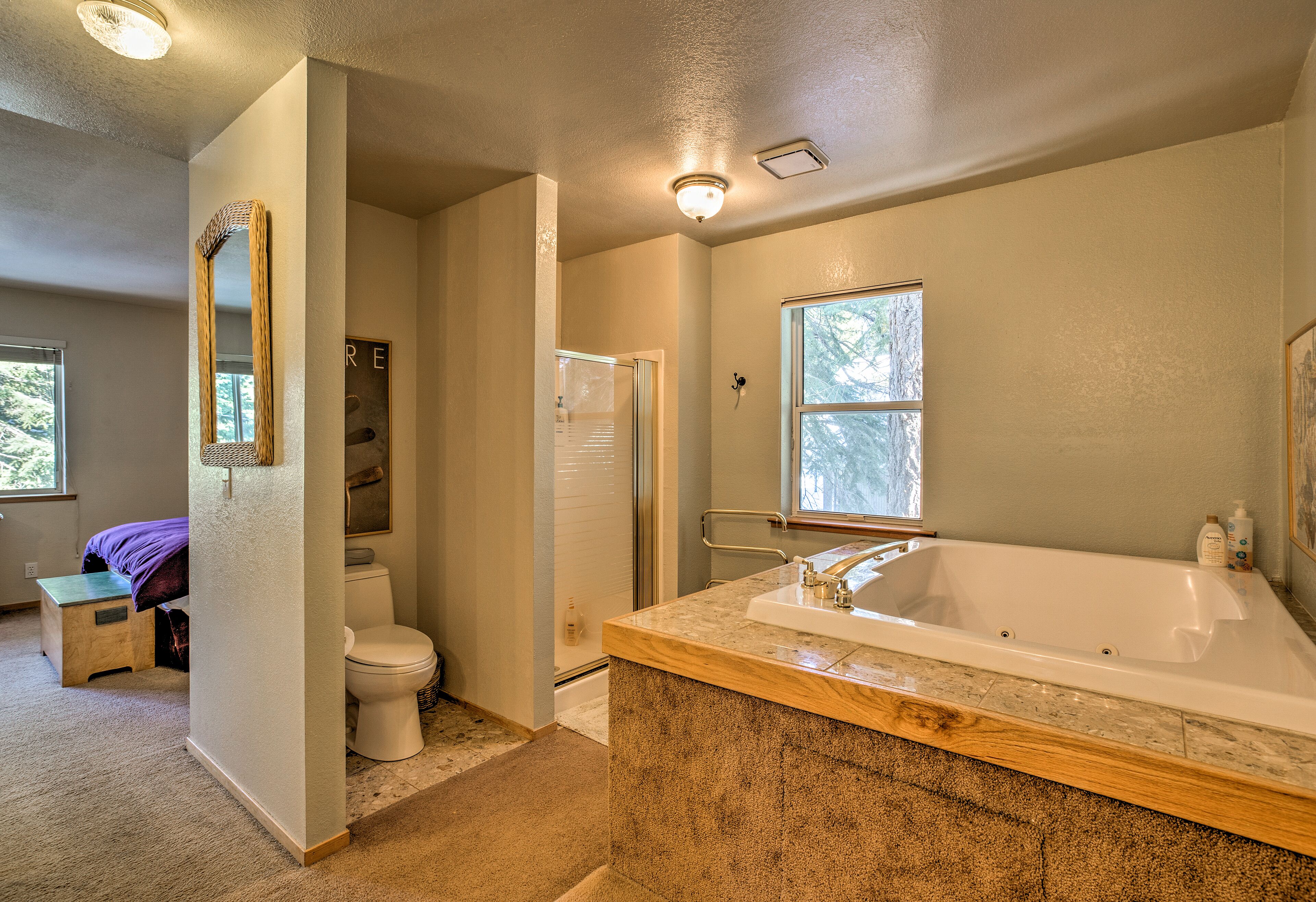 A bathroom with a large bathtub, a toilet, and a shower. There is a wooden bench and a small step stool near the toilet.