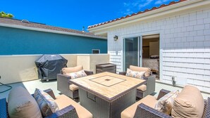 An outdoor patio with wicker furniture, a barbecue grill, and a glass door leading to a room.