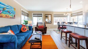 A living room with a blue sofa, a brown armchair, and a dining area with a kitchen counter and bar stools.