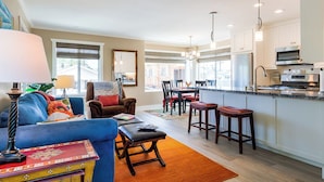 A modern living room with a blue sofa, a coffee table, and a dining area with a kitchen in the background.