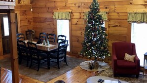 A cozy cabin interior with wooden walls, a dining area, a Christmas tree, and a red armchair.
