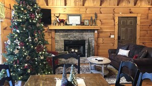 A cozy log cabin interior with a decorated Christmas tree, a fireplace, and rustic wooden furniture.