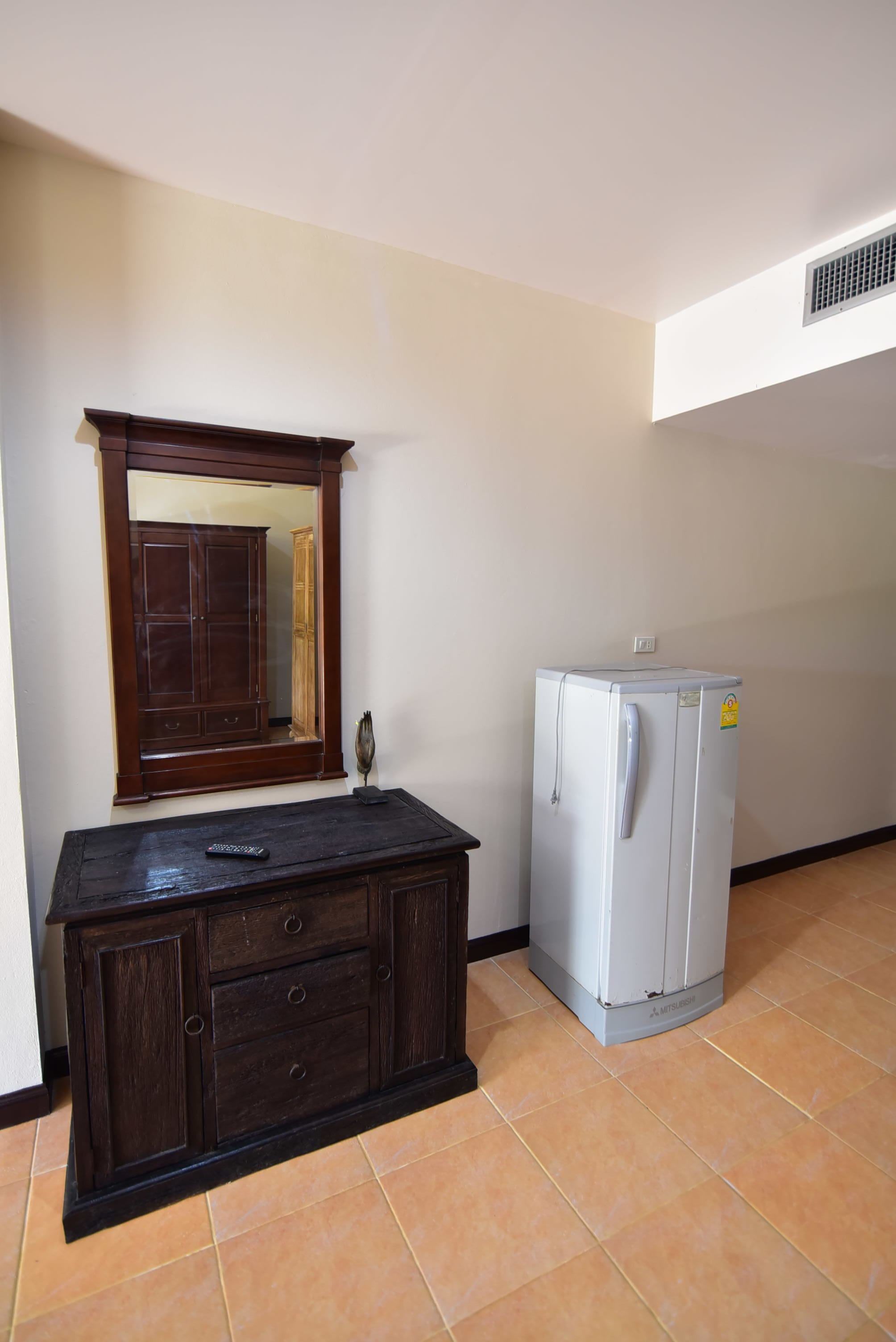 A room with a dark wooden dresser, a white refrigerator, and a large mirror on the wall.