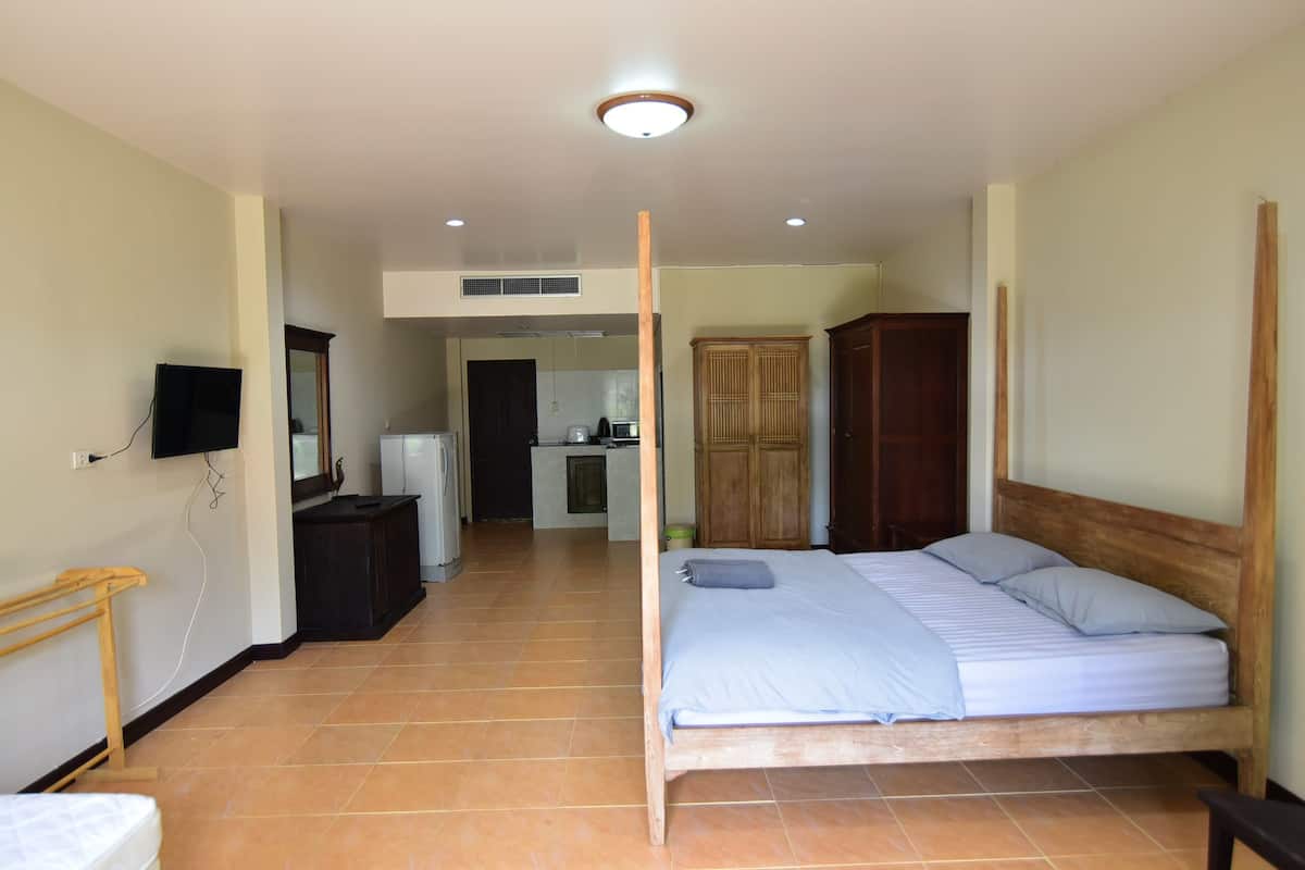 Quarto com cama de madeira, uma pequena escrivaninha, televisão e guarda-roupa.