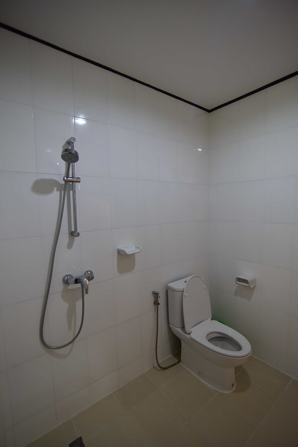 A small, clean bathroom with white tiles, a toilet, a shower with a handheld showerhead, and a soap dish. - Baan Chai Lay Apartment (Ko Lanta)