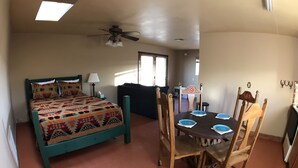 A room with a bed, a dining table with chairs, a ceiling fan, and a window.