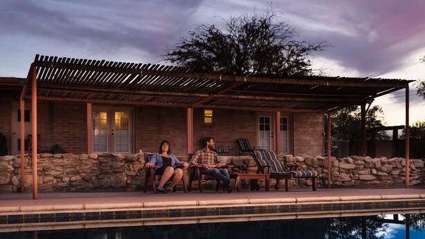 A poolside area with a covered patio, stone walls, and a view of the sky.