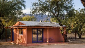 A small, single-story building with a metal roof, a covered porch, and a sliding glass door.