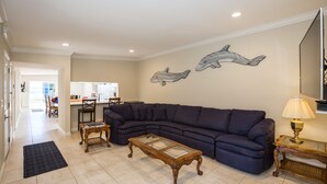 A living room with a sectional sofa, a glass-top coffee table, and a wall-mounted lamp. - Huntington Beach Furnished Home,  Private Patio, Bikes, Parking & Putting Green (Huntington Beach)