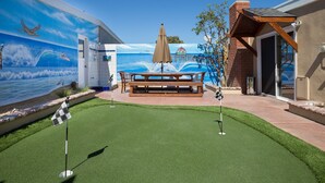 A pool area with artificial grass, a wooden bench, and a mural of a beach scene. - Huntington Beach Furnished Home,  Private Patio, Bikes, Parking & Putting Green (Huntington Beach)