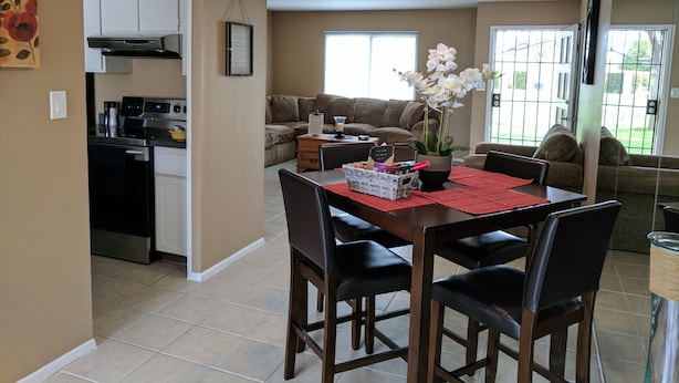A dining area with a table, chairs, and a red placemat. There is a kitchen area with appliances and cabinets. The room has beige walls and a large window with blinds. - Complete retreat with private hot tub. (Scottsdale)