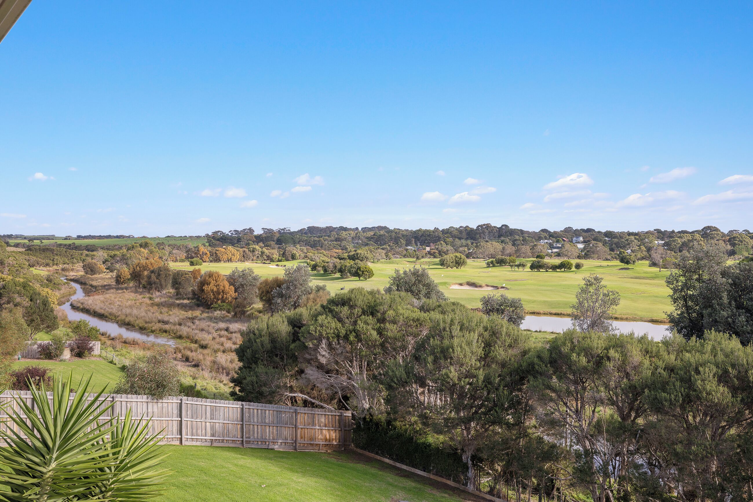 A view of a golf course with a river, trees, and a wooden fence.