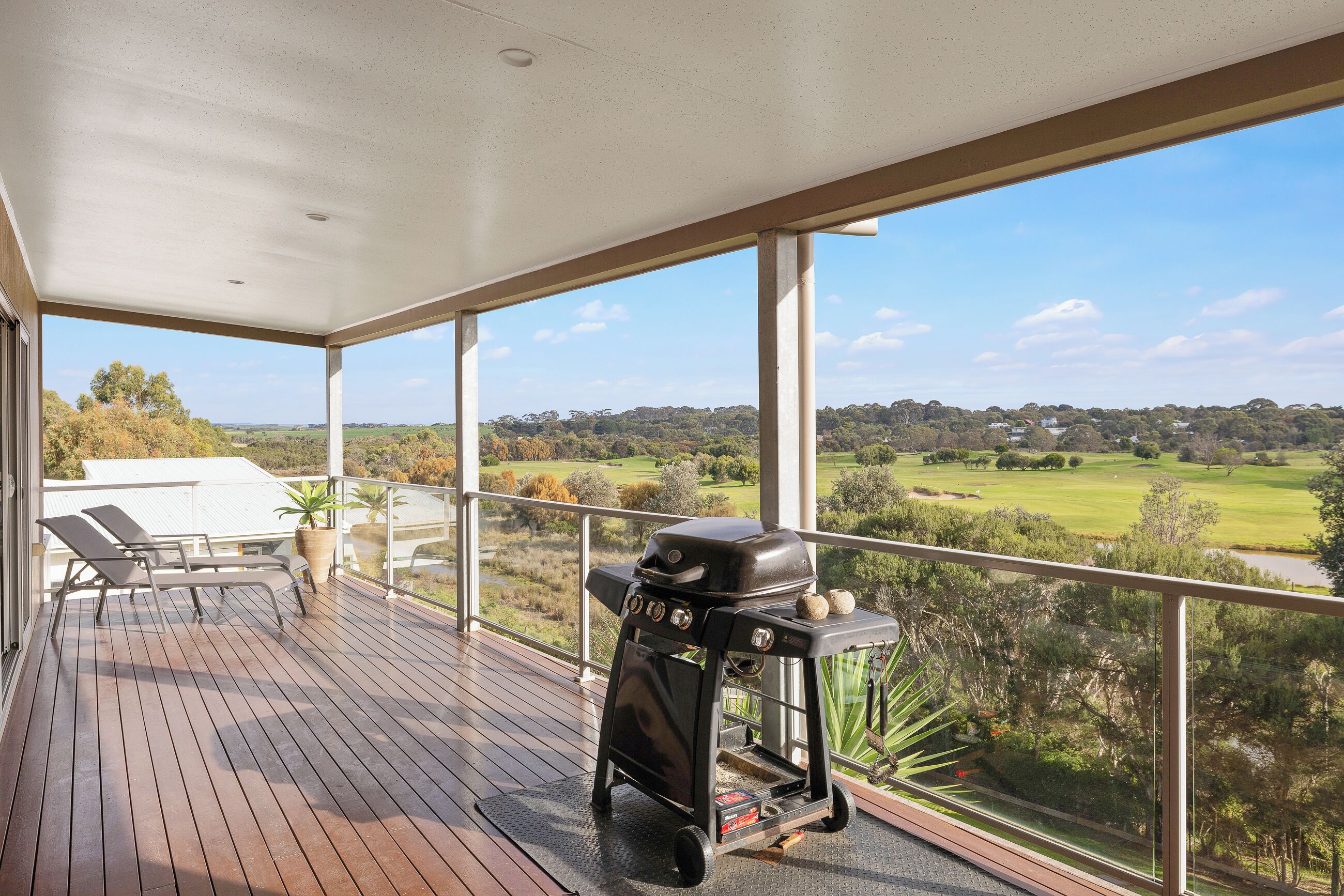 A covered outdoor area with a barbecue grill, lounge chairs, and a view of a golf course.