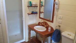 Un baño con tocador de madera, un lavamanos blanco, grifo dorado, un espejo, toallero y un inodoro.