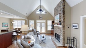 A spacious living area with a high ceiling, a stone fireplace, and a dining area with a bar. - 5 BDRM Beautiful Peaceful Lake Front Home 3 Kings, 1 Queen, 4 Twins, Pool, Spa (Greensboro)