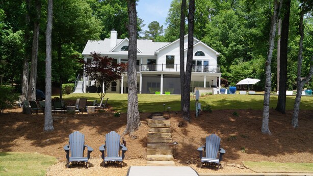 A lakeside property with a dock, Adirondack chairs, and a large house with a covered porch. - 5 BDRM Beautiful Peaceful Lake Front Home 3 Kings, 1 Queen, 4 Twins, Pool, Spa (Greensboro)