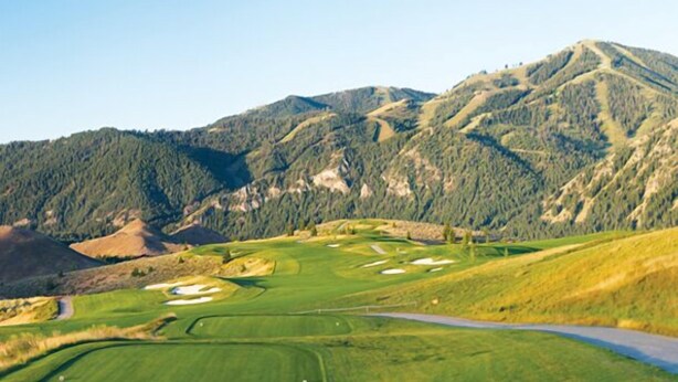 A golf course with a road running alongside it, surrounded by forested mountains. - Great 1 (plus) bedroom condo. This is the best location in Ketchum! (Ketchum)