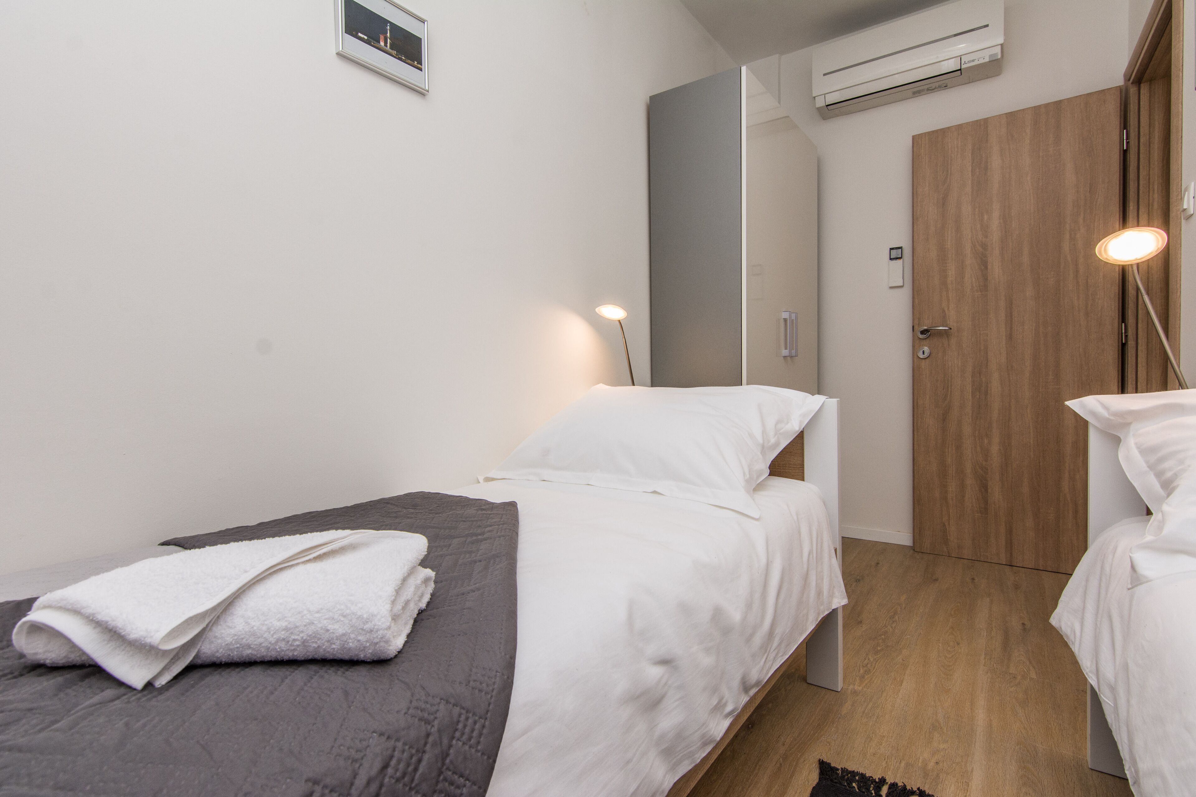 A small, modern bedroom with a single bed, a bedside table, a mirror, and a wardrobe.