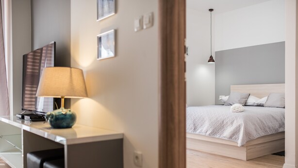 A modern hotel room with a bed, a desk with a lamp, and a television.