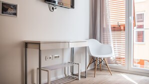 A modern room with a white desk, a white chair, a TV mounted on the wall, and a window with blinds.