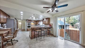 A spacious kitchen with wooden cabinets, a central island with bar stools, a ceiling fan, and a sliding glass door leading to a backyard.