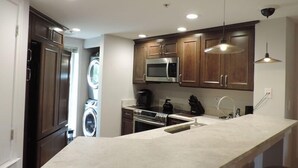A modern kitchen with wooden cabinets, a built-in microwave, a stainless steel range, and a large island with a sink.