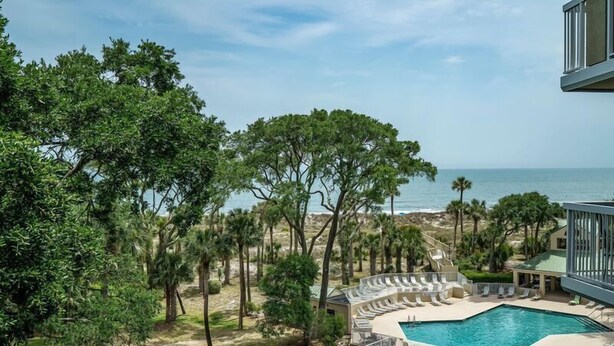A pool area with lounge chairs and a view of the ocean.